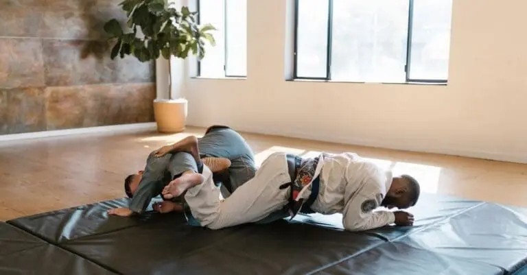 Two individuals practicing ground grappling and submission techniques on a mat during an adult self defense class.